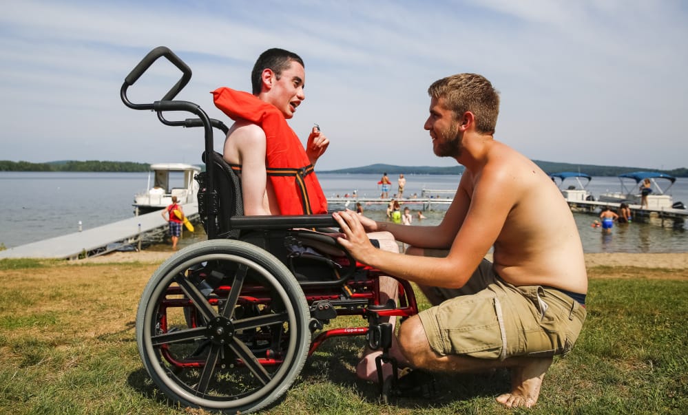 Andrew Artrip, left, and camp counselor Alex Schofield confer before they enter the water together at Pine Tree Camp in Rome. According to U.S. Census data, 16 percent of Maine residents – 206,000 people – have some physical disability, compared to 12 percent nationally.